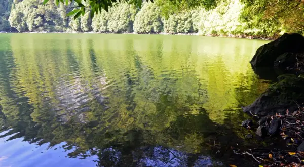 Reflejos verdes y azules en la serena Lagoa do Congro, rodeada de exuberante vegetación y rocas cubiertas de musgo.