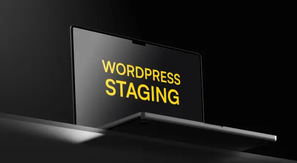 Laptop z napisem "WORDPRESS STAGING" na ekranie, w ciemnym otoczeniu.