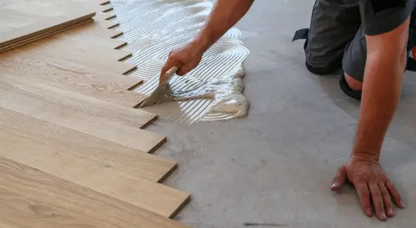 Un operaio stende la colla per posare un nuovo pavimento in legno. Scopri quanto costa rifare il pavimento.
