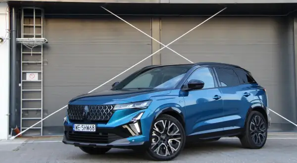 Błękitny Renault Austral 2025 z czarnym dachem i felgami stoi przed szarą, nowoczesną bramą.