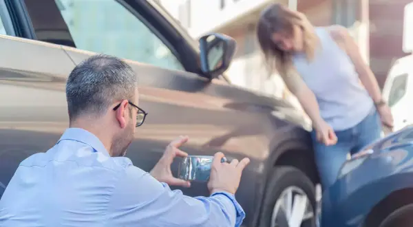 Man fotograferar parkeringsskada. Kvinnan undersöker skadan, en parkeringsskada smitning.