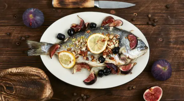 Un filet de dorade rôti, garni de figues, olives et citrons, prêt à être dégusté.