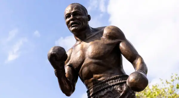 Bronze statue of boxer Jersey Joe Walcott in a fighting stance against a blue sky with clouds.