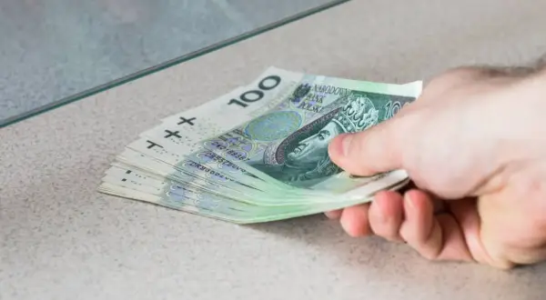 Dłoń przekazuje stos banknotów 100 zł. To przykład, co to depozyt bankowy – pieniądze wpłacane do banku.