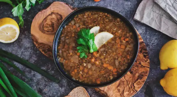 Herzhafte italienische Linsensuppe mit Karotten und Sellerie, garniert mit Zitrone und Petersilie, daneben Brot und frische Kräuter.