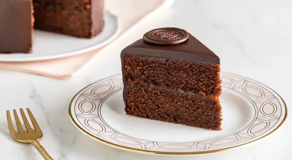 Una fetta di torta Sacher, con la sua glassa lucida e il ripieno di marmellata, mostra i suoi deliziosi ingredienti.