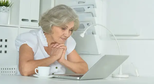 Starsza pani z zaciekawieniem patrzy na laptopa, szukając informacji, ile trwa staż z urzędu pracy.
