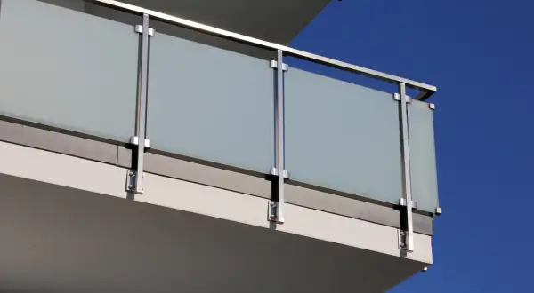 Nowoczesne mocowanie balustrady od czoła z matowego szkła i stali nierdzewnej na tle błękitnego nieba.