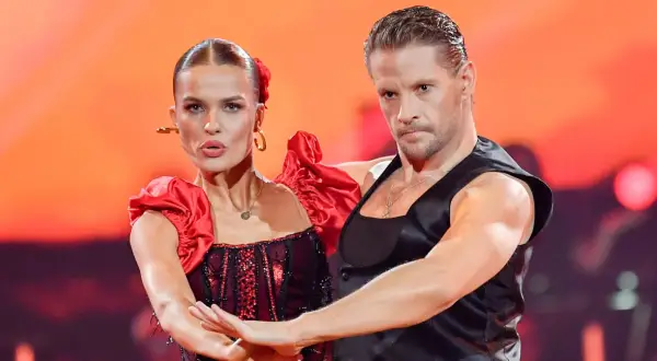 Para tańczy w strojach inspirowanych folklorem. Kobieta w czerwonej sukni z falbankami, mężczyzna w czarnej kamizelce.