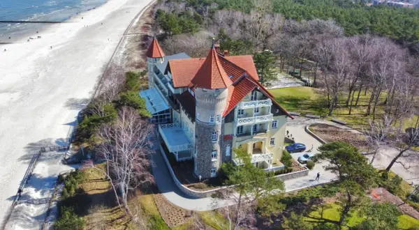 Elegancki budynek z czerwoną dachem i wieżą, blisko piaszczystej plaży i morza.