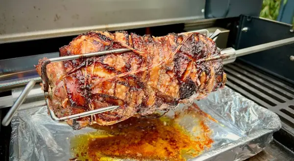 Ein saftiges, am Spieß gebratenes Stück Fleisch, das nach Porchetta aussieht, tropft in eine Aluschale.
