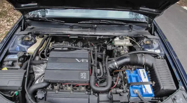 Silnik V6 wolnossący w samochodzie Peugeot. Widać akumulator Varta i elementy układu dolotowego.