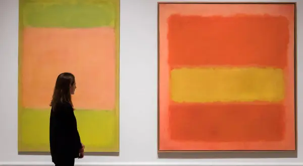 Kobieta podziwia abstrakcyjne dzieła sztuki obrazy Rothko: zielono-pomarańczowy i pomarańczowo-żółty.