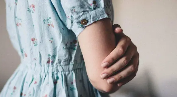 Een vrouw in een bloemenjurk houdt haar arm vast, misschien om oefeningen tegen trillende handen te doen.