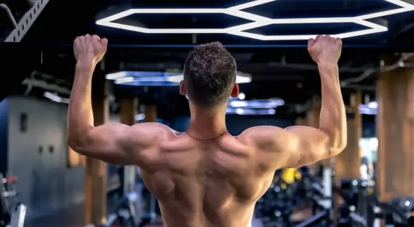Mężczyzna wykonuje ćwiczenie scapular pull ups na drążku, budując silne plecy i ramiona w nowoczesnej siłowni.