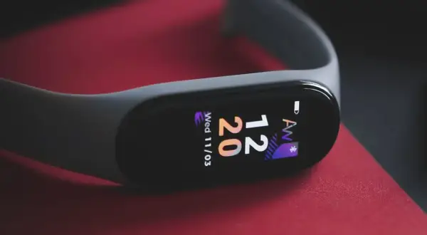 Szary smartband do pływania na czerwonym tle. Wyświetla godzinę 12:20 i datę.