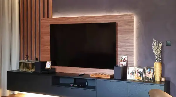 Nowoczesny salon z telewizorem w zabudowie meblowej. Drewniane panele i subtelne podświetlenie tworzą przytulną atmosferę.
