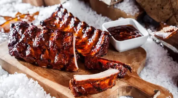 Saftige spareribs im backofen, glasiert und mit BBQ-Sauce, auf einem Holzbrett mit Schnee dekoriert.