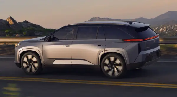 Srebrny Toyota Highlander jedzie po drodze z górzystym krajobrazem w tle. Sprawdź aktualną toyota highlander cena!