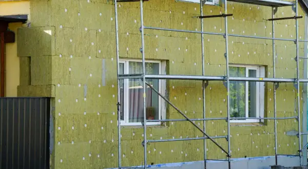 Lavori in corso per pulire muro esterno con cappotto isolante. L'edificio è circondato da ponteggi metallici.