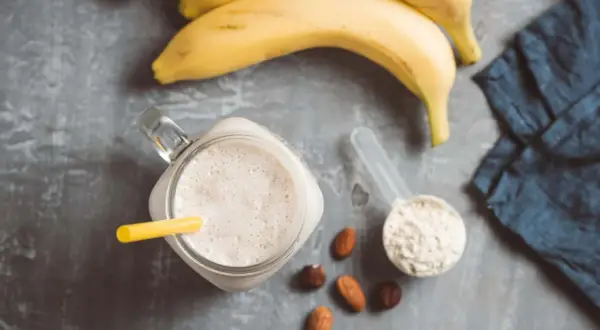 Ein cremiger Proteinshake mit Banane und Nüssen, daneben eine Schaufel Proteinpulver, bereit für das Training. Kreatin im Proteinshake für mehr Power.