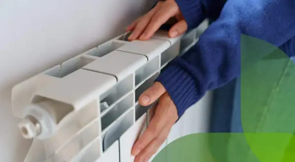 Mani che toccano un termosifone bianco, suggerendo come svuotare un termosifone per la manutenzione.