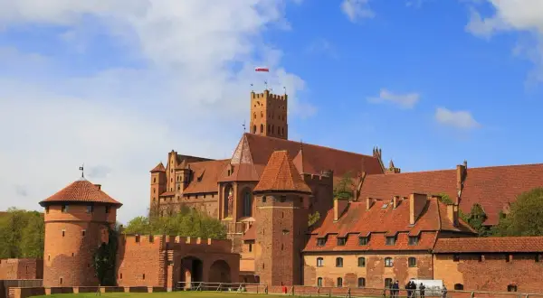 Imponujące zamki do zwiedzania w Polsce: ceglana twierdza z wieżami i czerwonymi dachami pod błękitnym niebem.