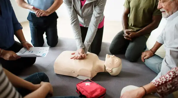 Persone in cerchio praticano RCP su un manichino. Si impara da chi sono designati gli addetti al primo soccorso.