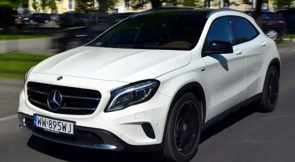 Biały Mercedes-Benz GLA AMG pędzi ulicą, jego sportowy wygląd podkreślają czarne felgi i przyciemniany dach.