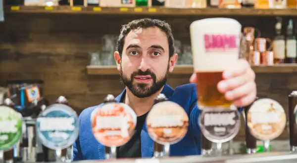 Barista con una birra in mano, pronto a versare nei bicchieri. Dietro di lui, una selezione di birre artigianali.