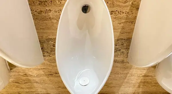 Nowoczesne pisuary o nietypowym kształcie, zamontowane na marmurowej ścianie. Ich wysokość podejść jest ergonomiczna.