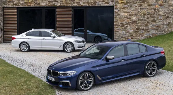 Dwa BMW, jeden granatowy, drugi biały, przed nowoczesnym budynkiem. Czy to xdrive co to za napęd?