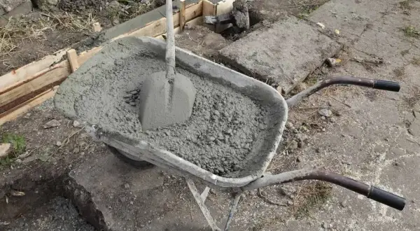 Taczka z betonem i łopatą czeka na wylanie zbrojenia ławy fundamentowej.