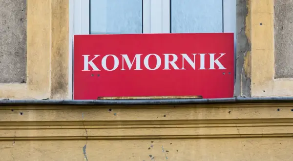 Czerwony szyld z napisem "KOMORNIK" nad oknem. Może to oznaczać, że komornik sądowy działa w tym miejscu, a kwota wolna od zajęcia jest chroniona.