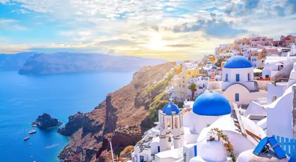 Widok na białe domy z niebieskimi kopułami na klifie nad morzem, Santorini, Grecja.