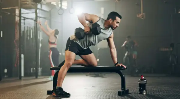 Mann mit shredded body trainiert im Fitnessstudio mit Hanteln.
