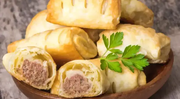 Stos pieczonego ciasta francuskiego z kiełbasą w środku, ozdobione natką pietruszki. Idealne na szybką przekąskę.