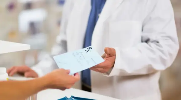 Farmaceuta w białym fartuchu podaje receptę. Dowiedz się, jak odzyskać kod recepty, aby zrealizować leki.