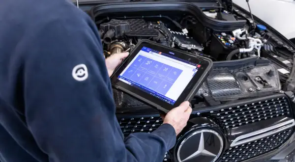 Tecnico esegue la revisione auto con tablet diagnostico, controllando i sistemi del motore.