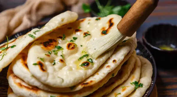 Frisch gebackenes Naan Brot, mit Butter bestrichen und mit Kräutern garniert, bereit zum Servieren aus der Pfanne.