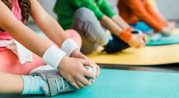 Dzieci ćwiczą, dotykając stóp. Delikatne ruchy mogą pomóc w przypadku hipermobilności stawów u dzieci.