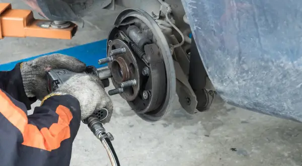 Mécanicien travaillant sur un tambour de frein usé. L'outil pneumatique est utilisé pour retirer les boulons de la roue.