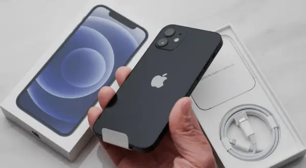 Czarny iPhone 12 w dłoni, obok pudełka i kabla. Dowiedz się, jak zrestartować telefon, gdy przestanie odpowiadać.