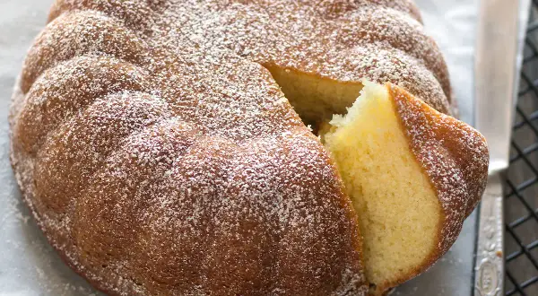 Una soffice torta allo yogurt, cosparsa di zucchero a velo, con una fetta tagliata che ne rivela l'interno dorato e profumato.