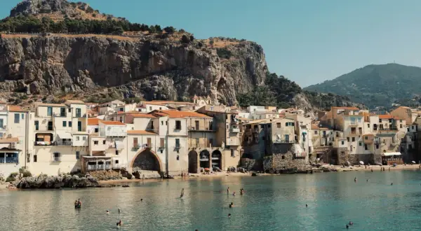 Un incantevole borgo da visitare in Sicilia, con case color pastello affacciate sul mare azzurro e una scogliera imponente alle spalle.