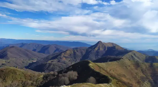 Panoramica mozzafiato del monte Matanna, con cime ondulate, boschi spogli e un cielo azzurro punteggiato di nuvole bianche.