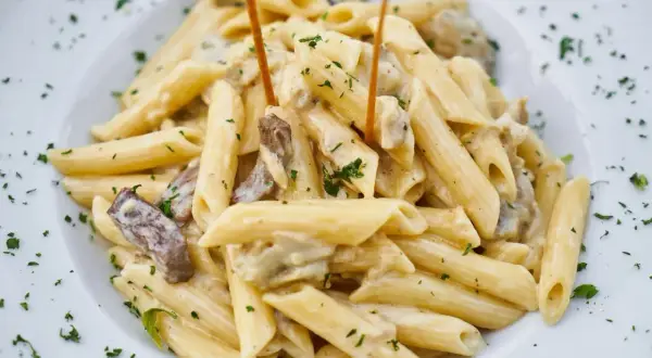 Penne w kremowym sosie z kawałkami mięsa i posypane natką pietruszki.
