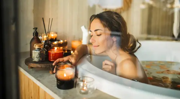 Entspannter beauty day zuhause: Frau genießt ein warmes Bad mit Kerzenlicht und duftenden Ölen.