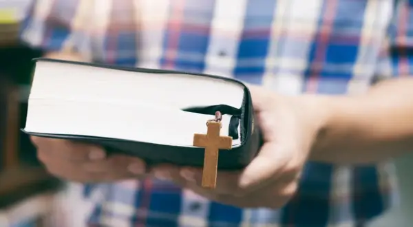 Osoba w kratę trzyma Biblię z drewnianym krzyżykiem, symbolizującym dwa przykazania miłości.