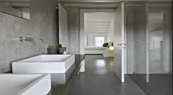 Salle de bain moderne avec murs en béton ciré, lavabos rectangulaires blancs et douche vitrée. La résine salle de bain offre un aspect brut et contemporain.